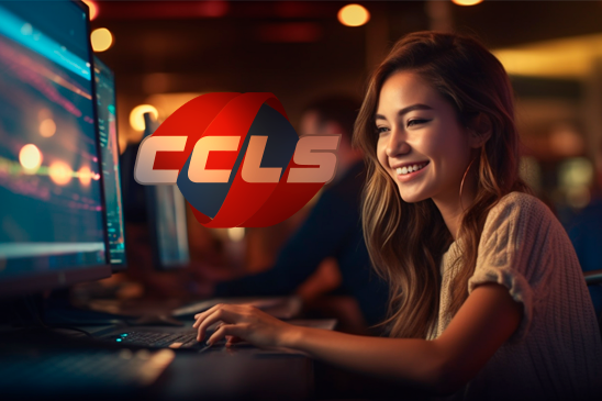 CCLS Class. Image description: Young woman smiling while using a computer in a room with CCLS logo on background.